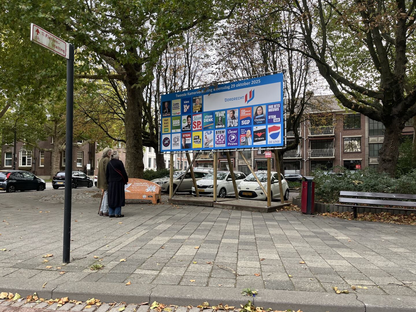 Two people looking at a huge billboard showing posters of political parties