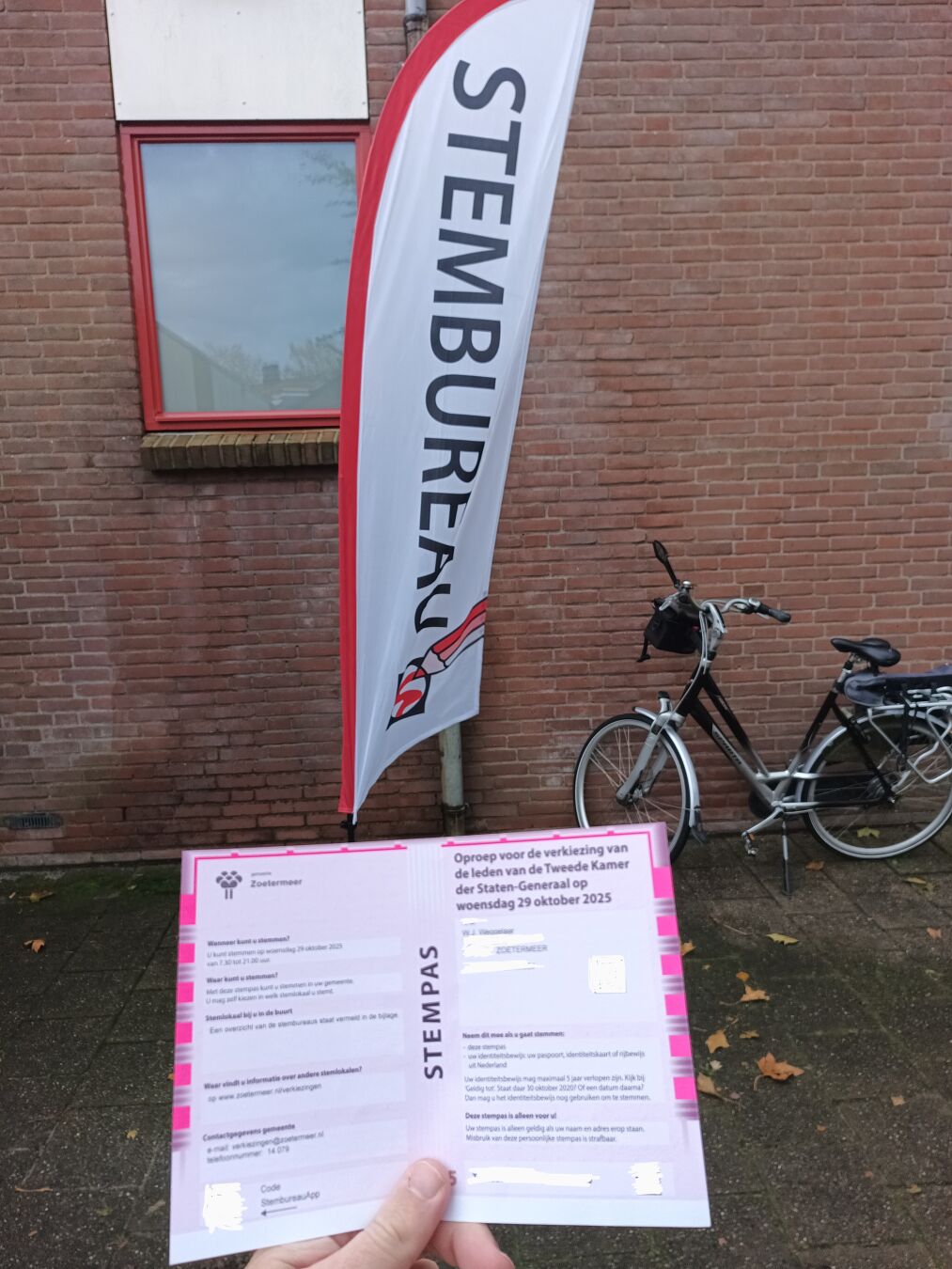 op de voorgrond mijn stempas met de vlag van het stembureau op de achtergrond