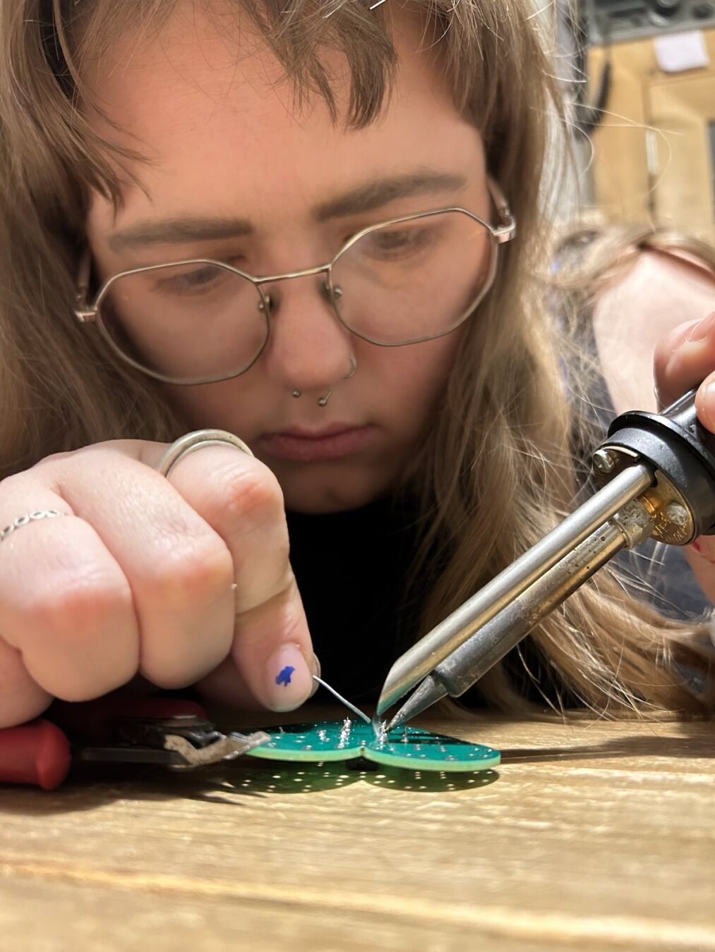 Close-up of Emily soldering a kit, holding the soldering iron and looking very focused