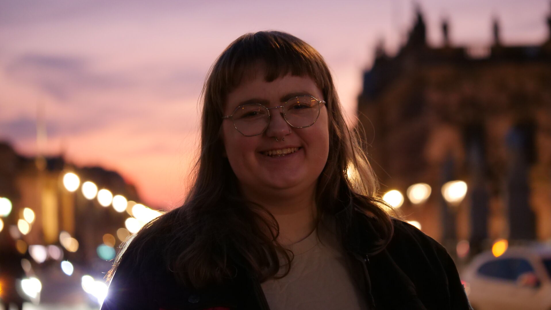 Portrait of emily smiling, with a blurred evening background. the light is very yellow and street lights are visible in the background