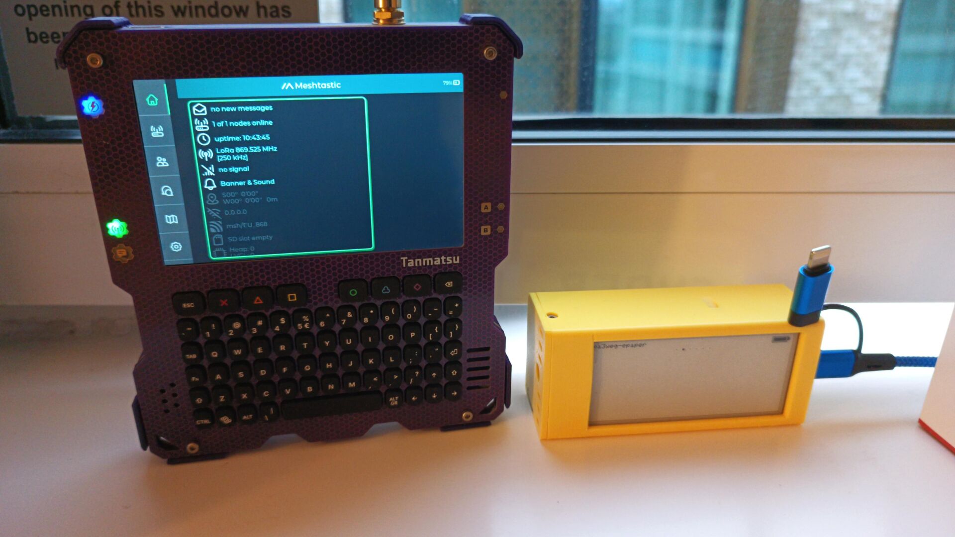 Tanmatsu (meshtastic) and Heltec (MeshCore) clients next to each other, both showing no clients other than themselves. the devices are next to a window in a hotel