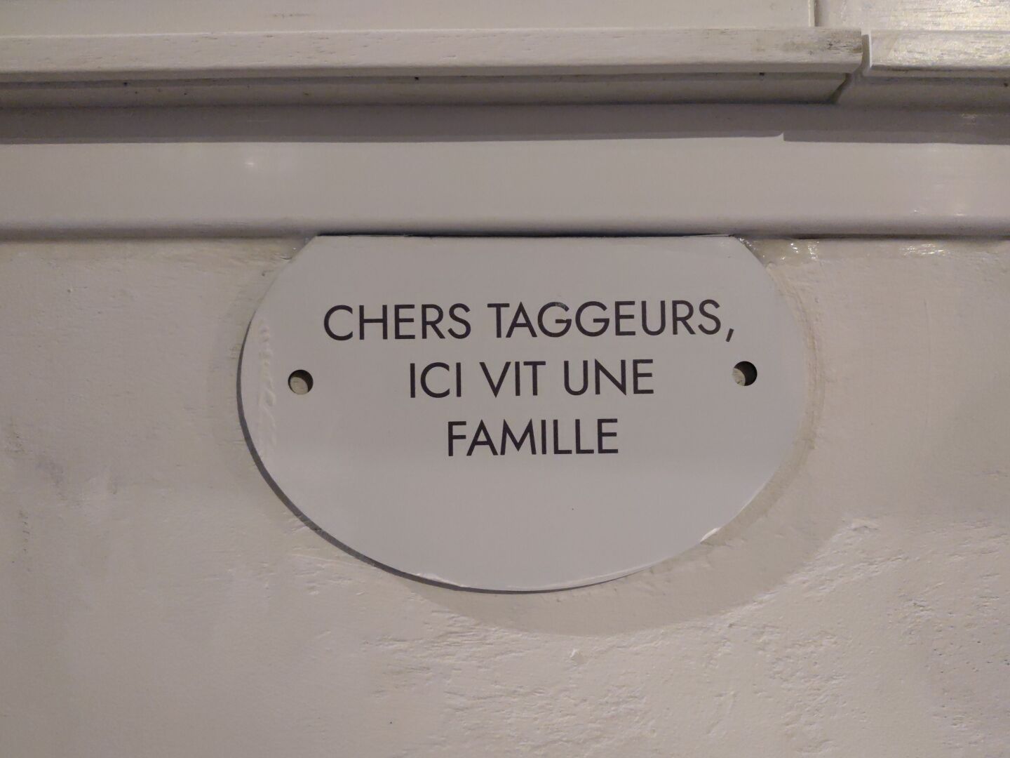 On a white wall a sign reading "chers taggeurs, ici vit une famille"